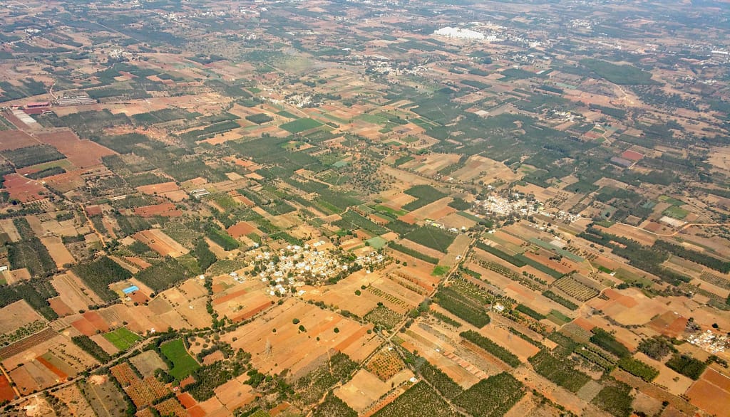 Aerial view of diverse agricultural landscape featuring cropland, villages, and greenery under daylight.