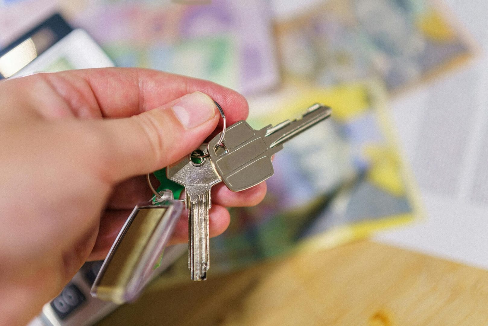 Close-up of keys in hand representing property ownership with blurred financial documents in the background.